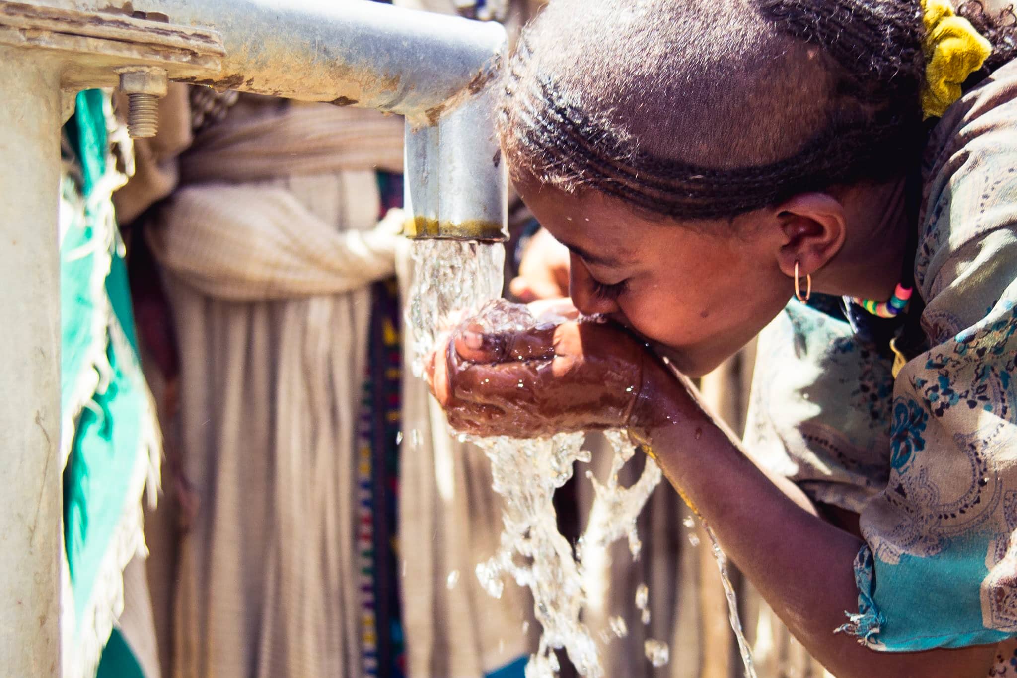 Ethiopian woman drinking from her cupped hand from a clean water pump.