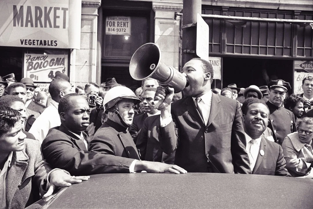 Dr. Martin Luther King Jr. speaking to a large crowd via megaphone.