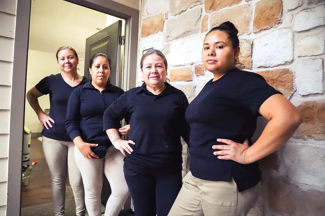 Four Latinx women in matching polo shirts and slacks, standing proudly in front of a Texas home for JUST.