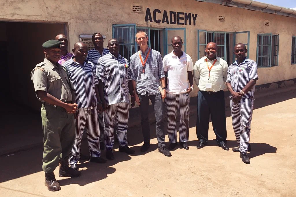 Justice-Defenders-Academy-Kevin-MIGHTY-ALLY Mighty Ally Co-founder and CEO Kevin Brown standing in a row of male prisoners in East Africa for Justice Defenders.
