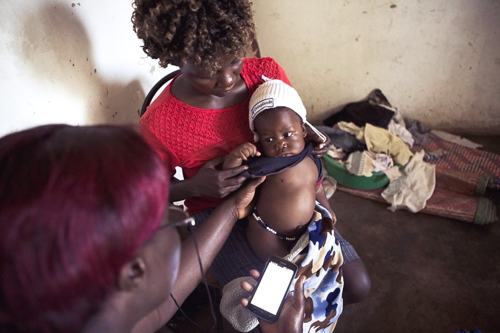 African mother holding her infant child while it is being examined by a doctor.