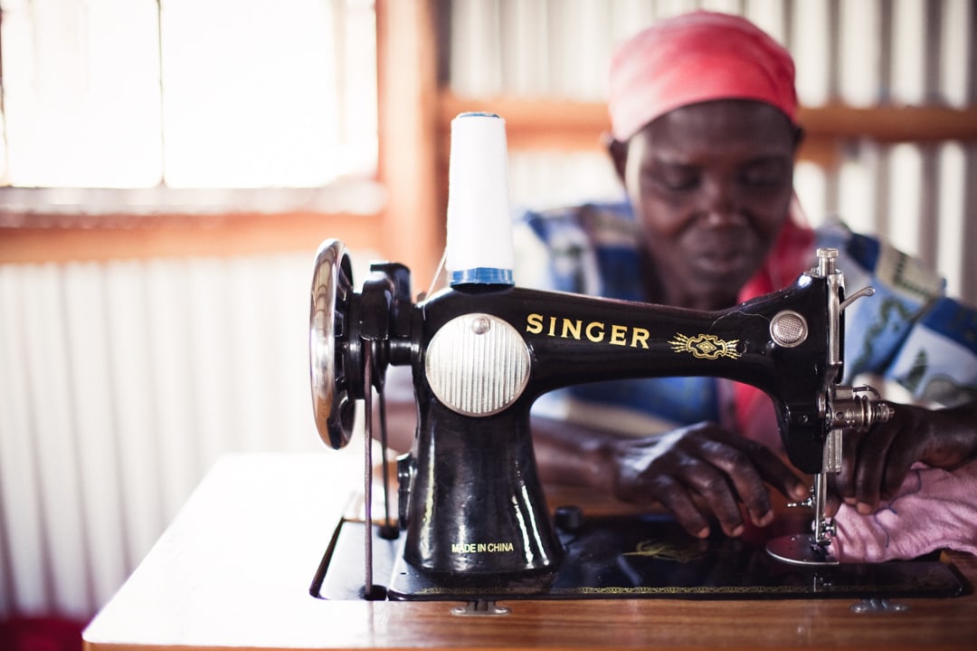 Kenyan woman sewing a garment on a manual black Singer sewing machine at Lwala Community Alliance.