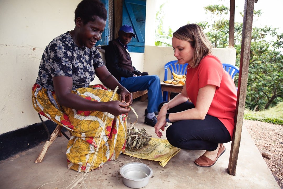 Mighty Ally co-founder Kathleen Souder crouched down learning from a Nyaka Granny about her basket weaving project in Uganda.