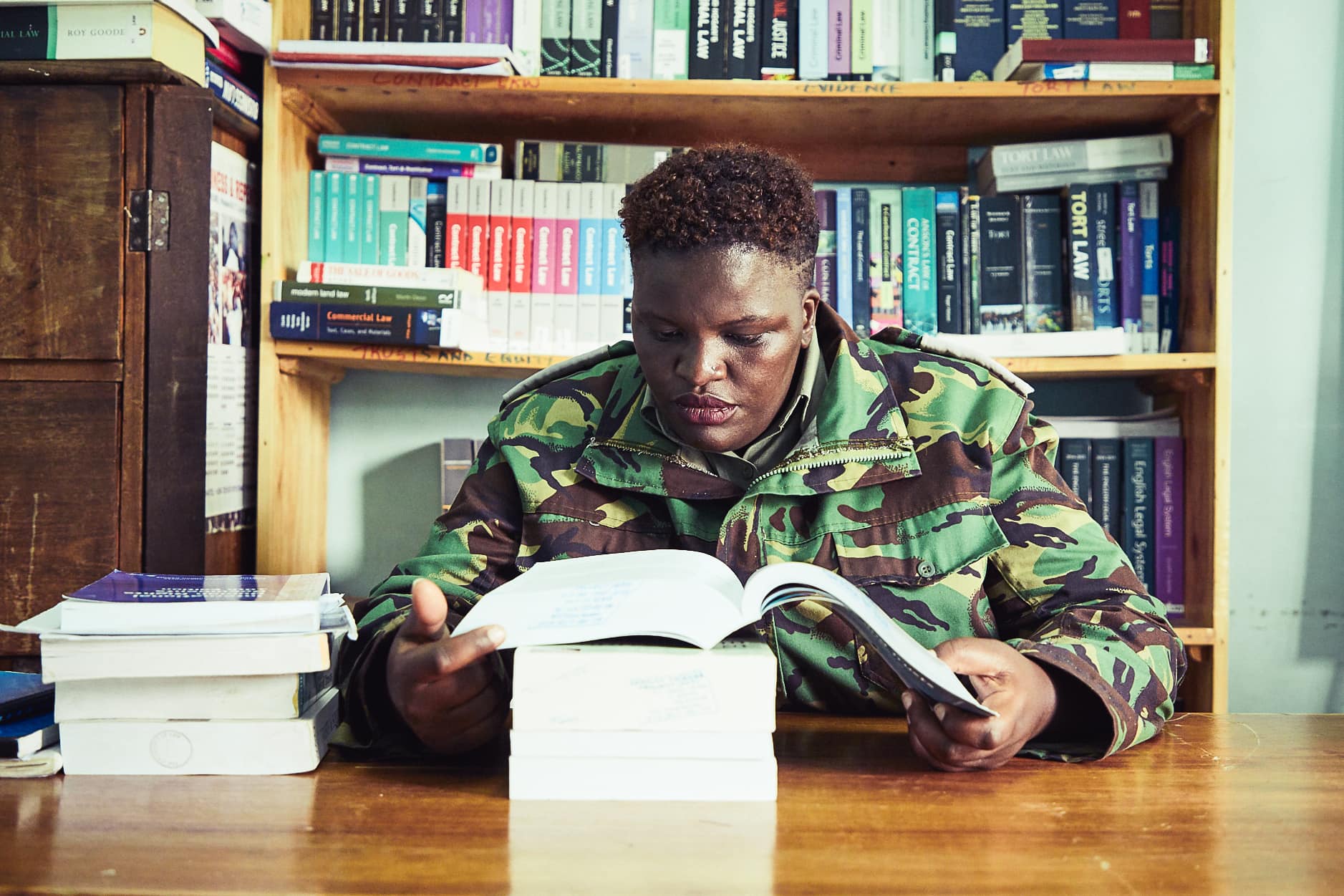 Black female prison guard in uniform studying a law book within a prison library