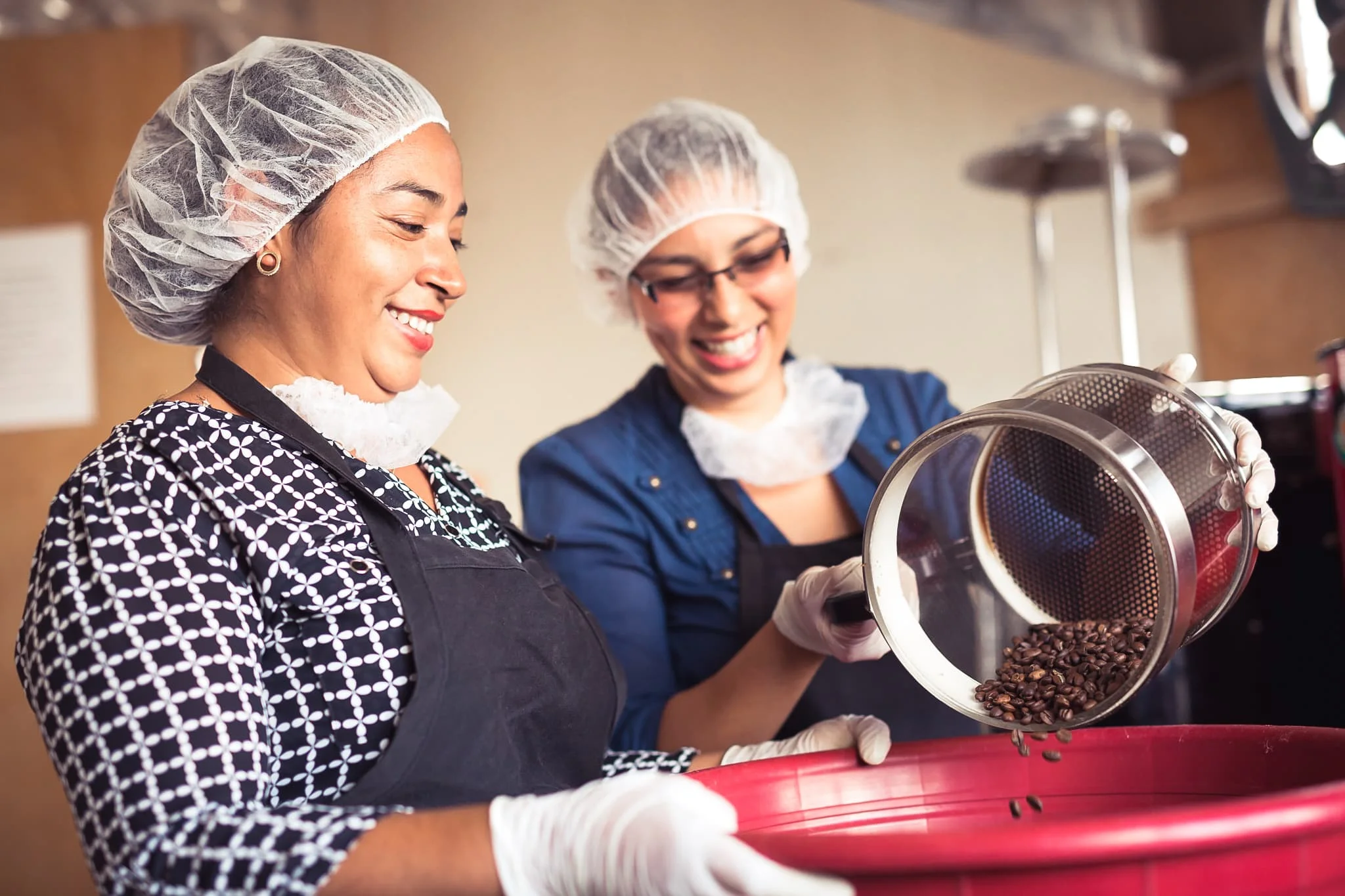 Two female Nicaraguan coffee farmers smiling at work while roasting a batch of coffee beans.