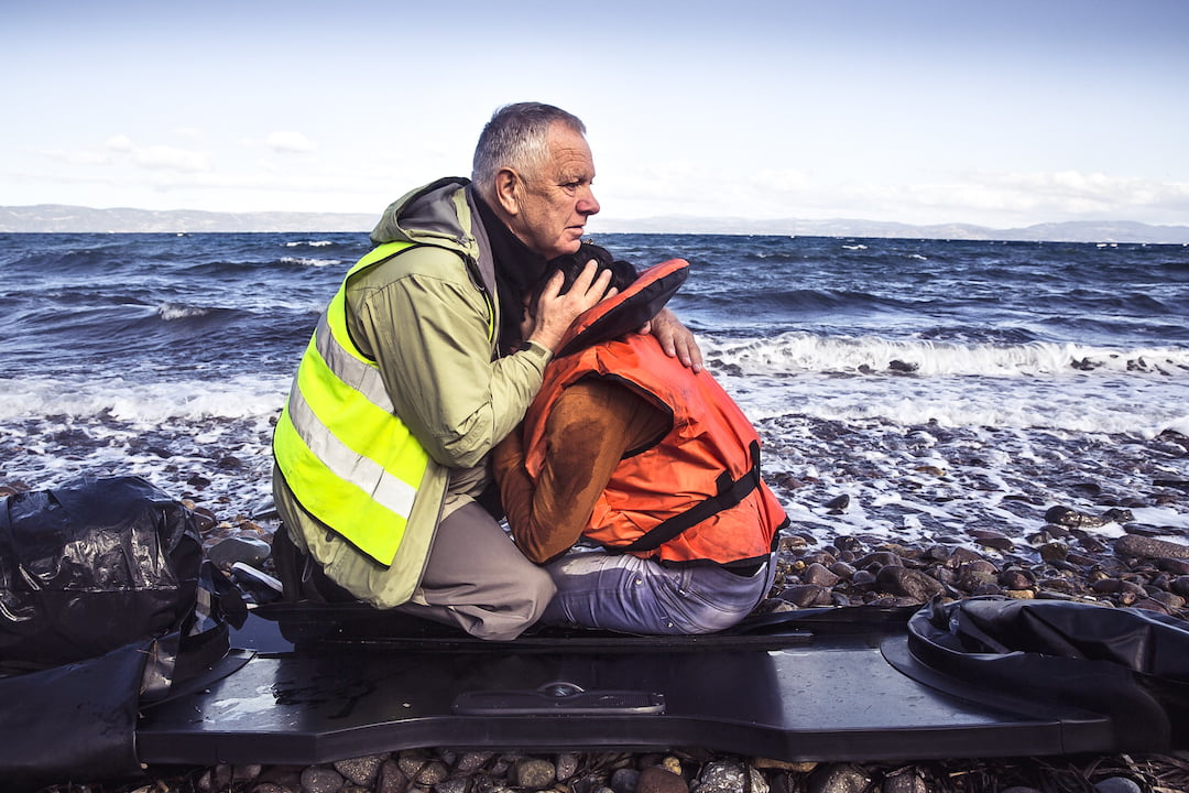 Man embracing child refugee on Greece shore upon his arrival by boat..