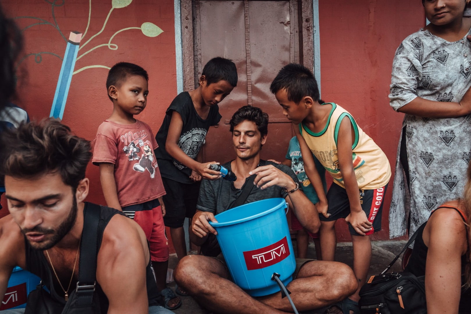 Man assisting three young boys to fit a water filter onto a bucket