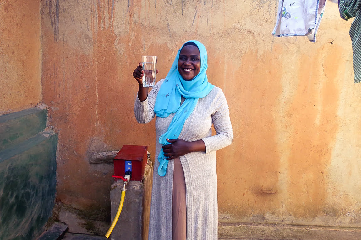 Woman holding clean glass of water drawn from a Water Access Rwanda tap.
