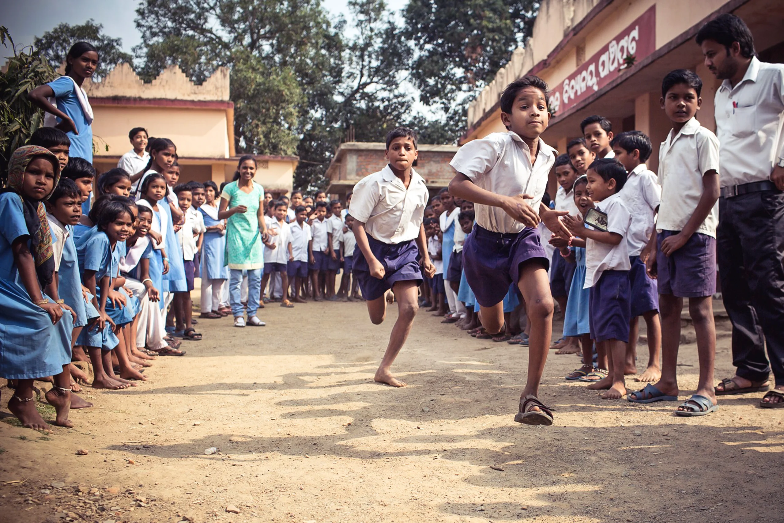 Two Indian boy students in school uniforms running a race in a crowd of peers.