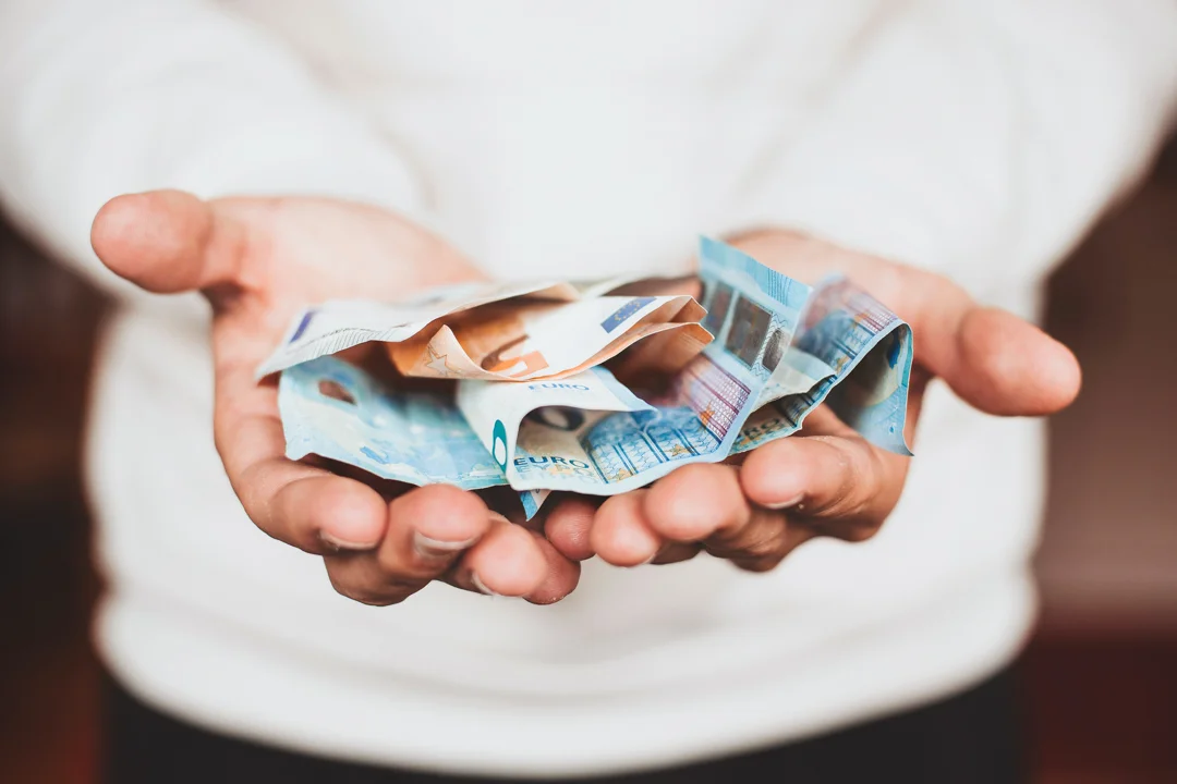 A pair of outreached hands, holding paper money.